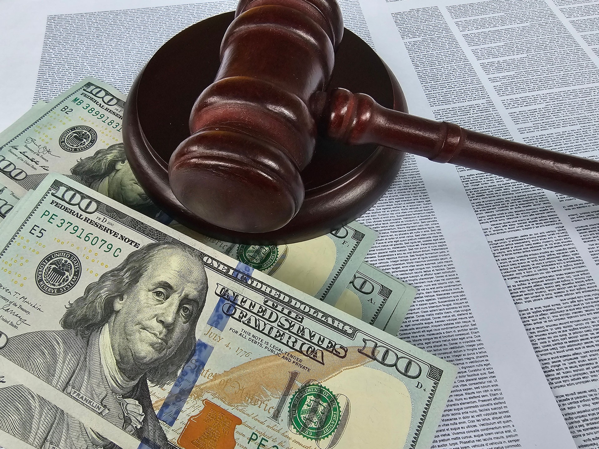 Court gavel resting on hundred dollar bills with legal documents in the background during a financial